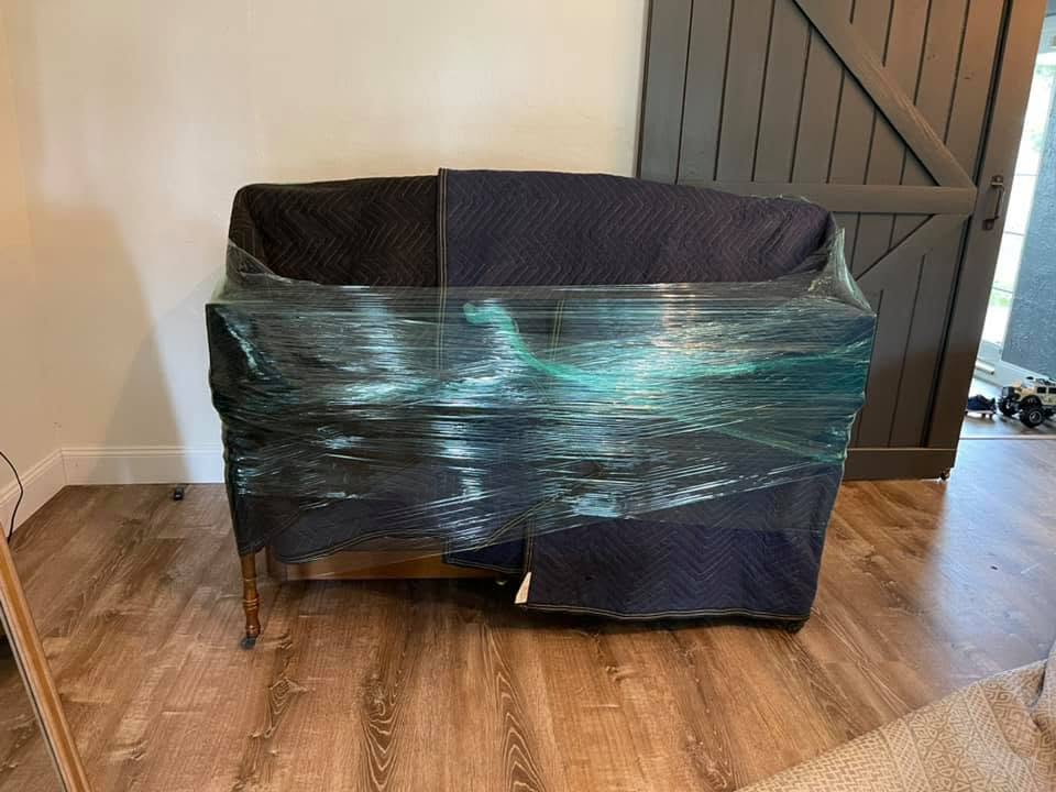 Piano wrapped in plastic moving wrap sitting on wooden floor indoors