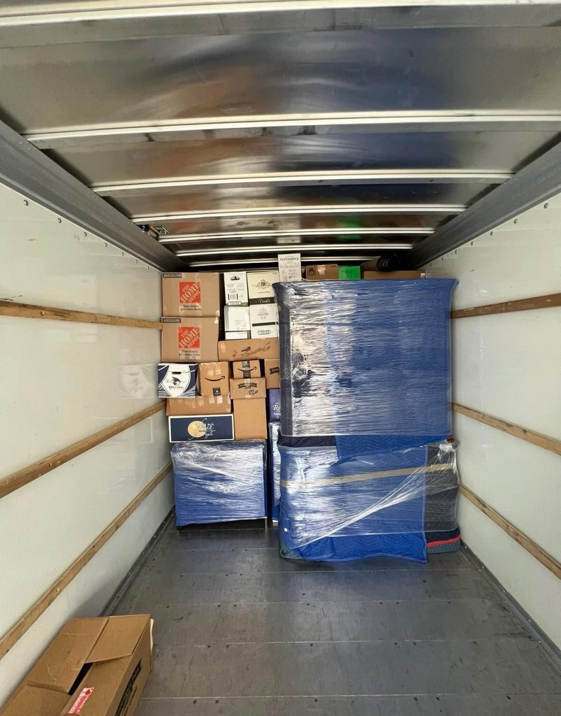Interior of moving truck loaded with cardboard boxes and blue wrapped furniture items